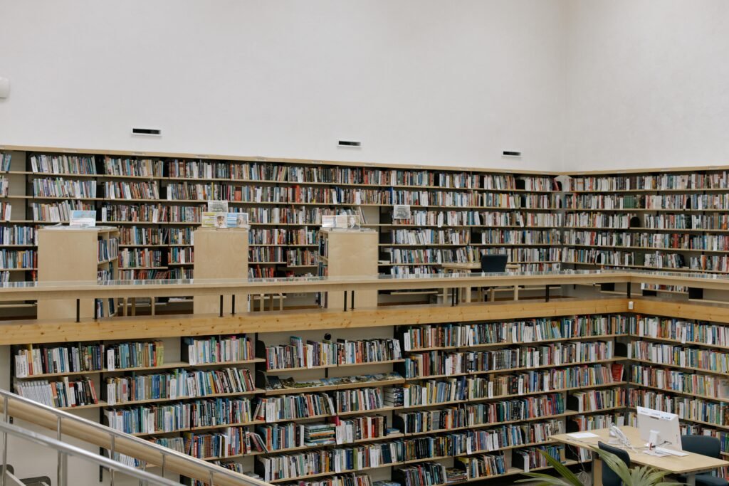 Spacious and well-lit modern library with multiple rows of book-filled shelves and reading tables.
